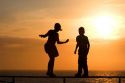 Silhouette of children walking on a railing at sunset by the sea.