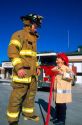 7 year old boy dressed in his home made Halloween costume as a firefighter, looks up to the real firefighter.