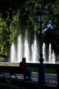 Man sitting on a park bench in front of a water fountain in Plaza Independencia in Mendoza, Argentina.