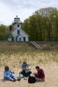 Family having a picnic on the beach in front of the Mission Point Light, a lighthouse located at the end of Old Mission Point, Michigan.