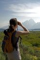 Woman viewing Mount Moran and Jackson Lake with binoculars in Grand Teton National Park, Wyoming.