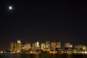 Boston skyline on a moonlight starry night with Boston Harbor in the foreground, Massachusetts, USA.