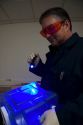 Fingerprint analyst using a colored light source to illuminate fingerprints on forensic evidence in a crime laboratory.