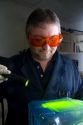 Fingerprint analyst using a colored light source to illuminate fingerprints on forensic evidence in a crime laboratory.