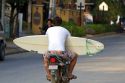 Man riding a scooter carries a surf board in the town of Tamarindo on the Northern Pacific Coast of Costa Rica.