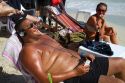 Man wearing head phones while sun tanning at Chaweng beach on the island of Ko Samui, Thailand.
