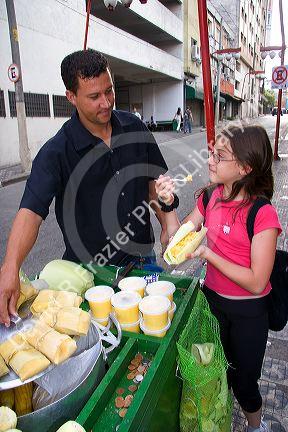 A young girl buying a corn snack from a street vendor in the Liberdade asian section of Sao Paulo, Brazil.