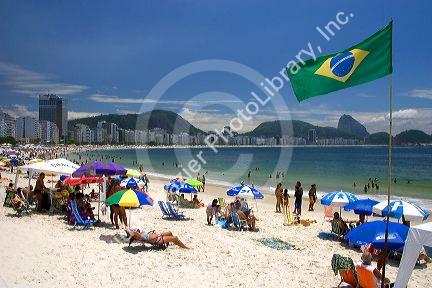 Visitors at the Copacabana Beach in Rio de Janeiro, Brazil and the flag of Brazil.