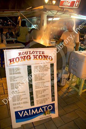 The menu board and cook for a roulotte, a food van in Papeete on the island of Tahiti.