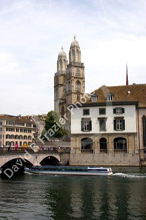 Tour boat passes beneath Munster Bridge crossing the Limmat River in Zurich, Switzerland with towers of Grossmunster church in background.switzerland, swiss, europe, european, travel, tourism, swiss alps, alps, alpine, zurich,  limmat river, grossmunster, church, boat, tour boat, munster bridge