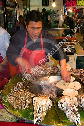 Vendor cooking cabeza tacos using a cazo at the Merced Market in Mexico City, Mexico.