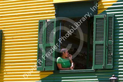 Woman standing in the window of a colorful building in the La Boca barrio of Buenos Aires, Argentina.