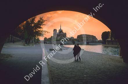 A couple walking along the Seine near Notre Dame at sunset in Paris, France.