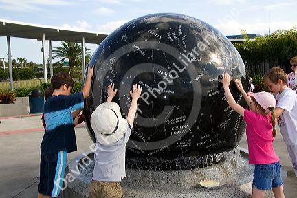 Children push the Constellation Sphere, a 9 ton granite sphere floating on water at the Kennedy Space Center Visitor Complex in Cape Canaveral, Florida.
