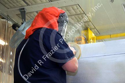 Manufacturing worker wearing protective safety gear while using a power sander on fire truck chassis at Spartan Motors in Charlotte, Michigan.