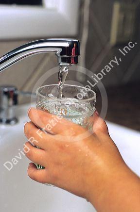 A child getting a glass of water from the kitchen faucet.