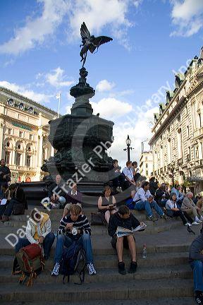 People sit on steps of the Shaftesbury Memorial Fountain in Piccadilly Circus, London, England.