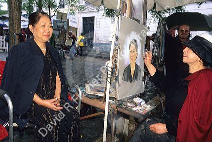 Sidewalk art at Montmarte area of Paris, France.  Asian artist paints portrait of Asian female.