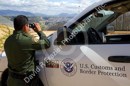 United States Border Patrol agent using binoculars to survey the new border fence that prevents illegal immagrant crossings at the U.S./Mexico border near San Diego, California