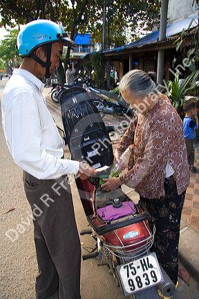 Vietnamese man purchasing one liter of gasoline from a woman on the street in Hue, Vietnam.