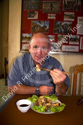 American man eating a spring roll with chopstix in Quang Tri Province, Vietnam.