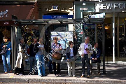 People wait at the Les Ecoles bus stop along Boulevard Saint-Michel in the Latin Quarter of Paris, France.