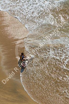 Mother and daughter sit on the beach in the surf at Acapulco, Guerrero, Mexico.