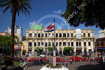 Costa Rican flag, red taxicabs, and yellow buses at the Parque Central in the city of San Jose, Costa Rica.