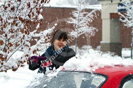 Woman brushing snow off of a car in Boise, Idaho, USA.