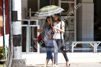 Burmese girls walk together under the shade of an umbrella in (Rangoon) Yangon, (Burma) Myanmar.