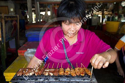Woman grilling satay at an open air market on the island of Ko Samui, Thailand.