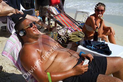 Man wearing head phones while sun tanning at Chaweng beach on the island of Ko Samui, Thailand.