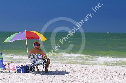 A senior citizen sitting under an umbrella at the beach in Clearwater, Florida.