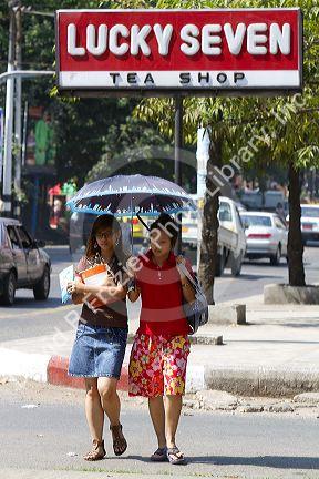 Teenage Burmese girls walk together under the shade of an umbrella in (Rangoon) Yangon, (Burma) Myanmar.