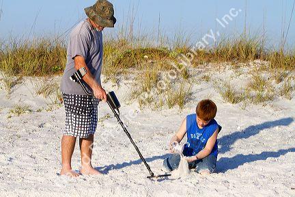 Father and son using a metal detector at the beach on the gulf coast of Florida, USA.