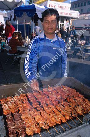 A man cooking meat in Thailand at street vending cart in Bangkok.
