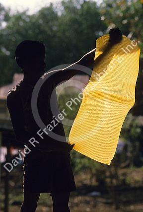 A sheet of processed latex backlit by the sun in Malaysia.  Worker inspects product prior to shipment.