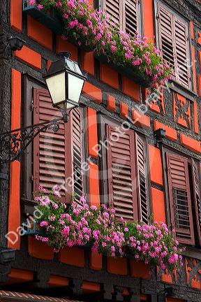 Red building with shuttered windows and flower boxes in the village of Ribeauville, Eastern France.