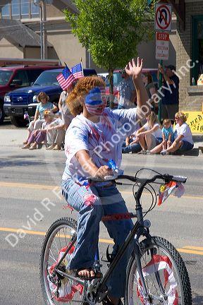 A girl with her face painted patriotic colors riding a bicycle in a small town Fourth of July parade in Cascade, Idaho.