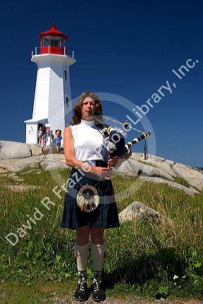 Scottish woman in traditional dress playing the bag pipes in front of a lighthouse at Peggy's Cove, Nova Scotia, Canada.